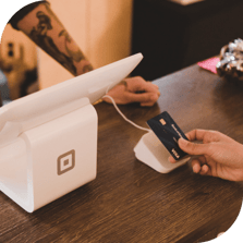 A cashier reaches across a counter to accept a Visa credit card from a customer