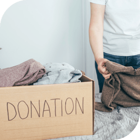 A person folds clothes to add to a box labeled "donations."