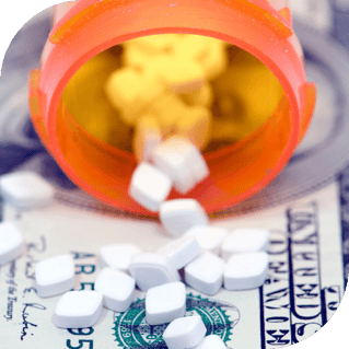 An open prescription bottle lays on its side with pills falling out on top of a $10 bill