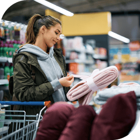 Person holding a blanket in a retail department store, considering making a purchase