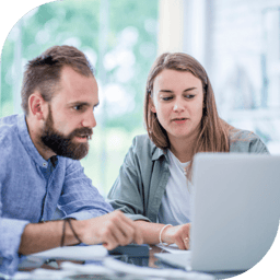 two colleagues sit side by side looking at a laptop