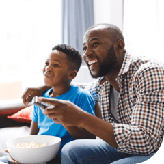 A father and son watch TV excitedly as they share a bowl of popcorn