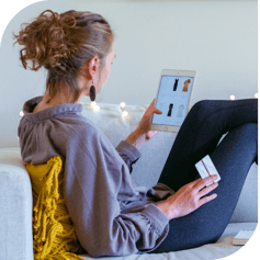 A woman reclines on a couch. She's holding a credit card in one hand and a tablet in the other. She is browsing a clothing store on her tablet.