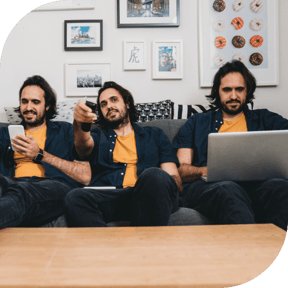 Three copies of a man in a yellow shirt sit side-by-side on a couch. One holds a smartphone, one holds a TV remote, and one uses a laptop.