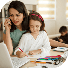 A young mother holds a phone to her ear while working on a laptop with her daughter in her lap. Her other child can be seen in the backgroun.